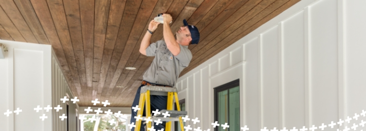 Technician on a ladder installing or repairing a ceiling light fixture on a wooden porch ceiling.