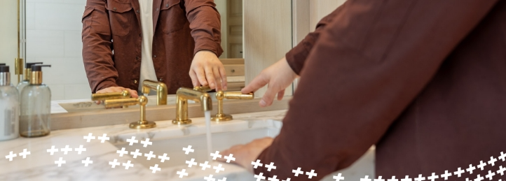 Man washing hands under a modern gold faucet in a bathroom sink.