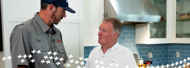 HVAC technician consulting with a homeowner in a modern kitchen about residential heating and cooling services.