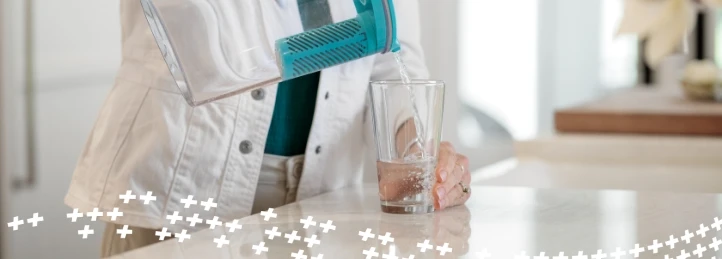 Person pouring filtered drinking water from a pitcher into a glass on a kitchen countertop.
