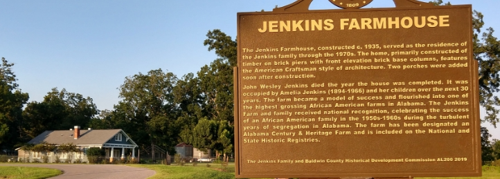Historical marker for Jenkins Farmhouse with farmhouse buildings and trees in the background.