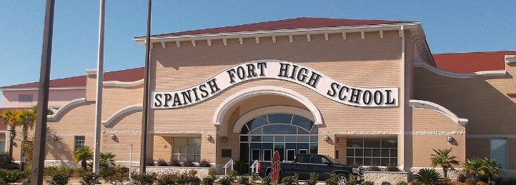Spanish Fort High School entrance with arched architecture and landscaped grounds under a clear blue sky.