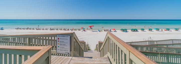 Beach access boardwalk leading to a white sandy beach with turquoise ocean water and beach umbrellas.