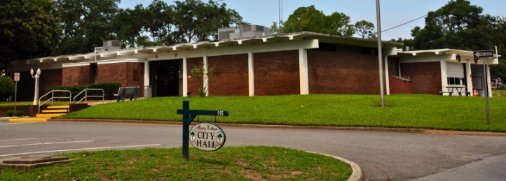 City Hall building with brick exterior, green lawn, and trees surrounding the municipal office.