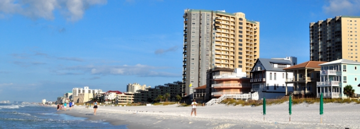 Beachfront skyline with high-rise condos, beachfront homes, and people walking along the sandy shore.