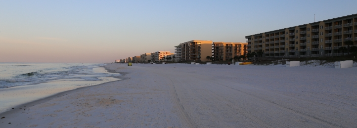Quiet sandy beach at sunset with beachfront condominiums and gentle ocean waves along the shoreline.