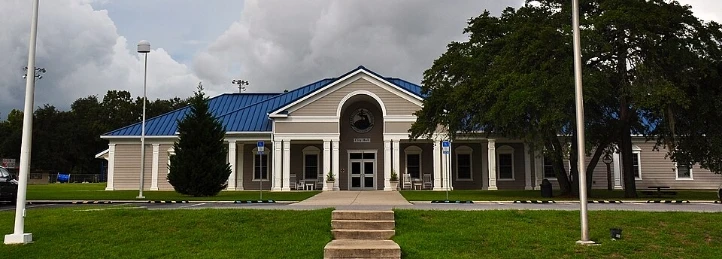 Community center building with a blue metal roof, manicured lawn, and trees under cloudy skies.