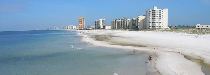 Panoramic beachfront view with white sand, calm ocean water, and high-rise condominiums along the shoreline.