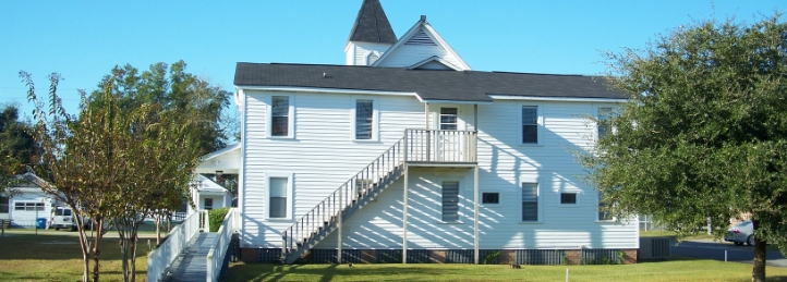 White church building with exterior staircase and steeple under a clear blue sky.