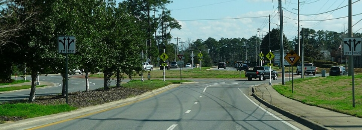 Multi-lane suburban road with traffic signs, turning lanes, and cars driving through a busy intersection.
