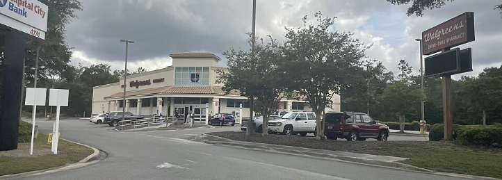 Walgreens pharmacy storefront with parking lot, cars, and roadside signage in a suburban area.