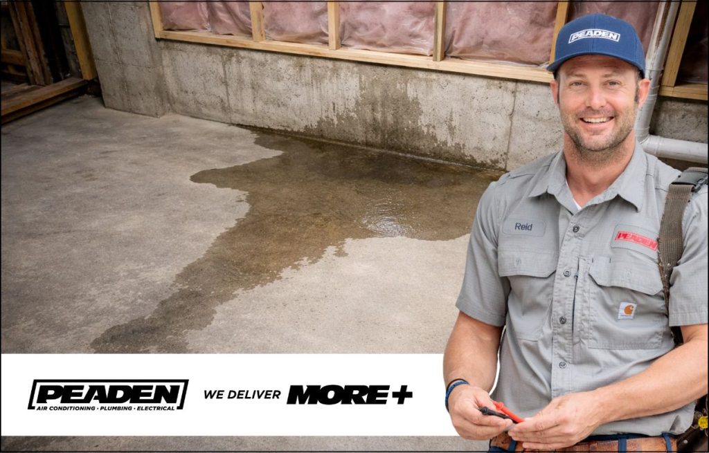 A noticeable slab leak on the basement floor with a PEADEN plumber standing looking at the camera