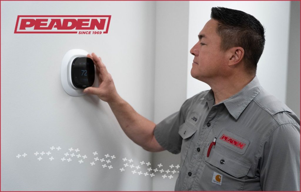 A Peaden HVAC tech adjusting a smart thermostat.